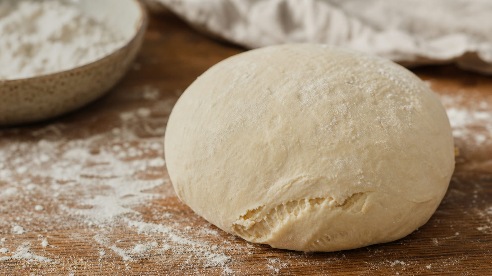 Close-up van een pizzadeegbal met een kleine scheur aan de rand op een met bloem bestoven werkblad