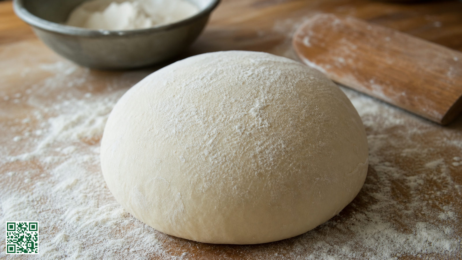 Bol pizzadeeg op een met bloem bestoven werkblad naast een kom en een deegschraper
