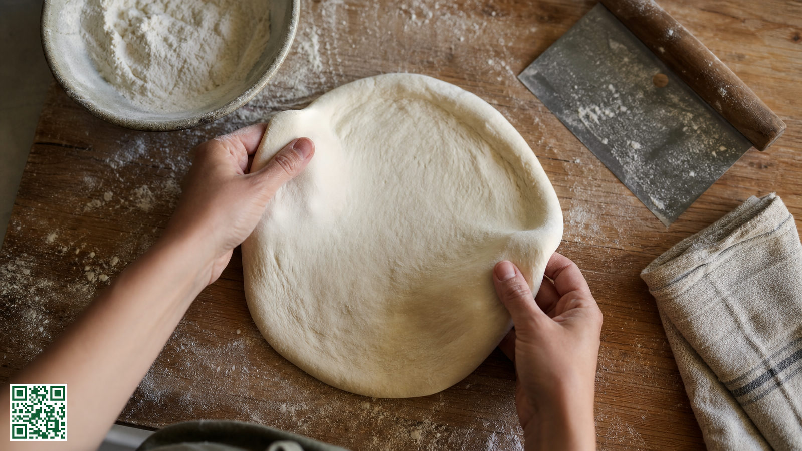 Handen die een ronde pizzadeegbol uitrekken op een bebloemd houten werkblad met een schaaltje bloem ernaast
