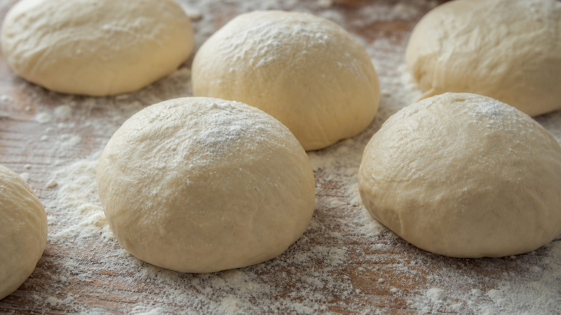 Meerdere deegbollen van verschillend formaat op een bebloemd werkblad