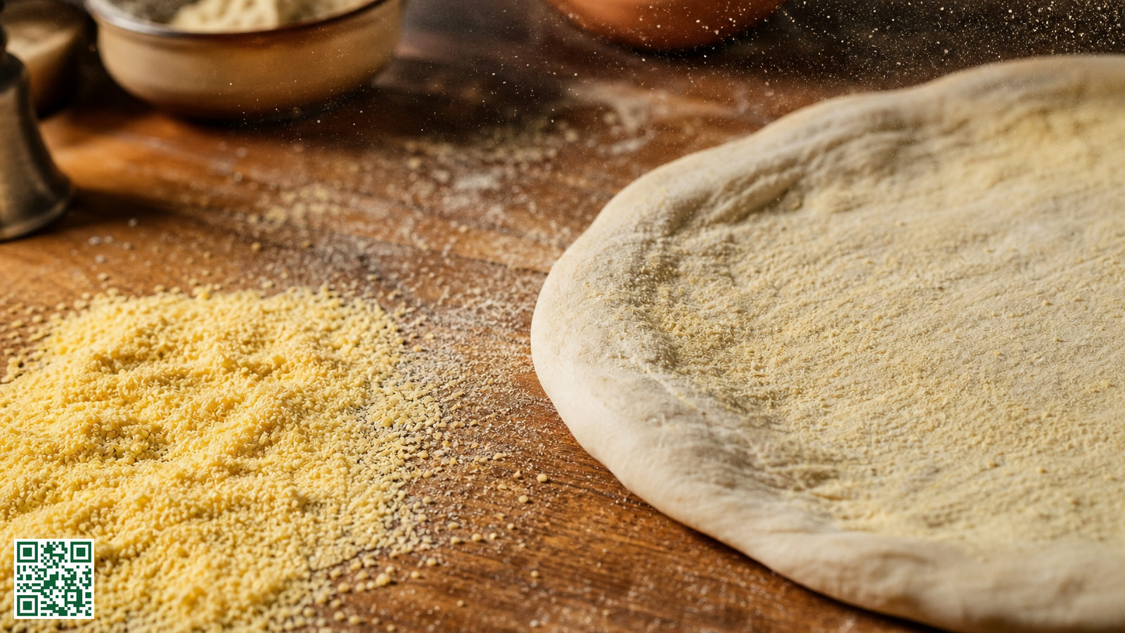 Grof geel semolina meel uitgestrooid op een houten werkblad naast een uitgerekte bol pizzadeeg